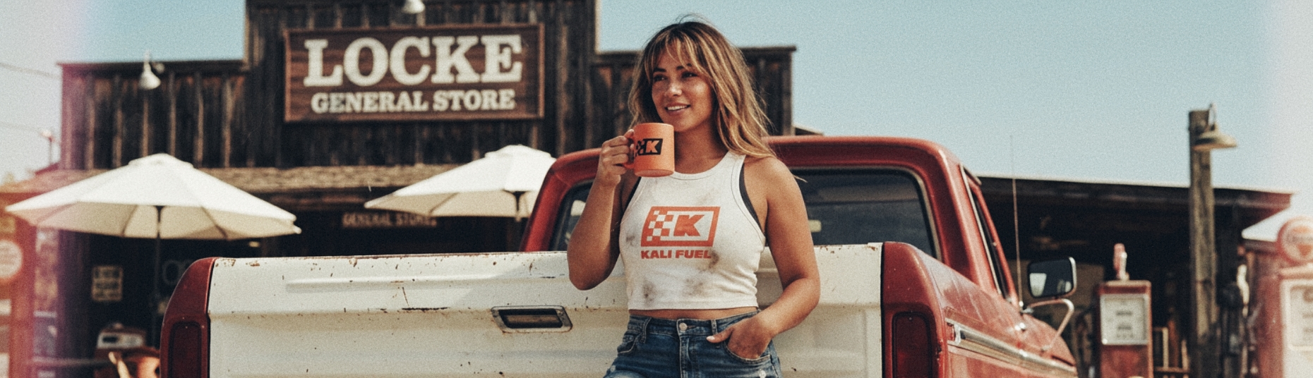 An image of a young woman enjoying a cup of coffee while leaning on the back tailgate of a classic ford pickup truck
